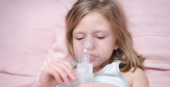 Portrait of sad little girl having inhalation for easing cough. Child in medical oxygen mask lying in bed. Labored breathing, lack of oxygen or inhalation concept