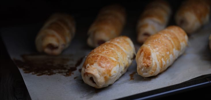 Close-up of homemade sausages in dough on baking sheet. Freshly baked sausage rolls. Lunch and yummy snack concept