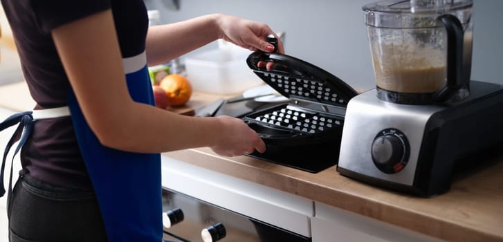 Close-up of woman preparing belgian waffle maker in kitchen. Waffle iron in kitchen. Preparing homemade waffles