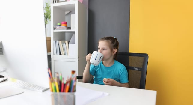 Portrait of little girl using laptop watch funny cartoons at home. Child drinking tea and eating cake. Home entertainment concept