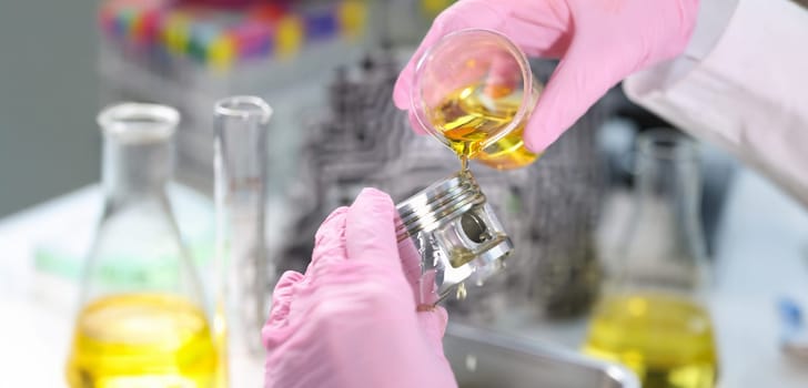 Close-up of person hand in gloves holding piston and pours lubricating oil on it. Mechanic fix car details. Lab, pit stop and service station concept