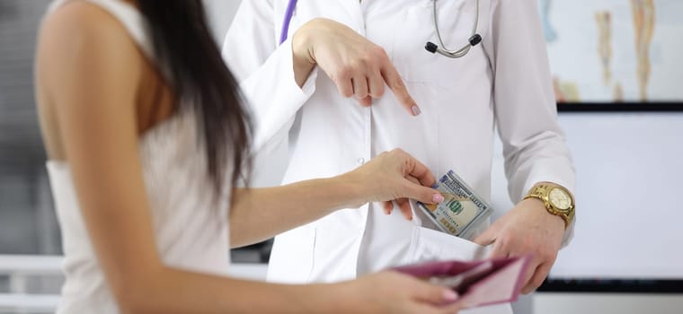 Close-up of female hand putting money to doctor pocket. Patient paying medical service. Bribe to practitioner. Corruption in medicine