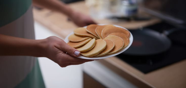 Close-up of female hands holding plate with tasty fresh homemade pancakes. Hot delicious meal for breakfast, nutritious food to start day. Food, eating concept