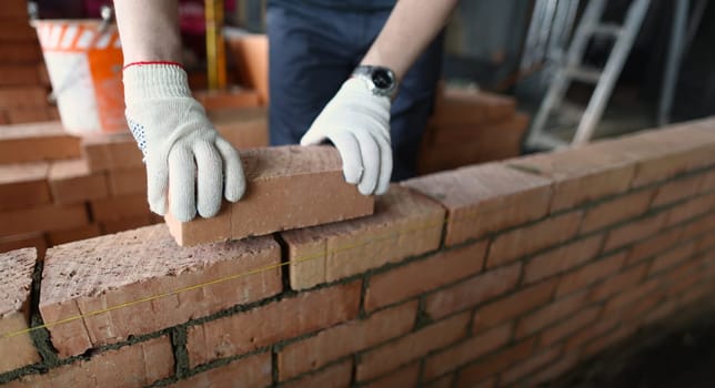 Close-up of male builder hands making make brickwork using red bricks. Builder building brick wall in house. Renovation and construction site concept