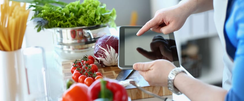 Close-up of vlogger chef showing ripe vegetables ingredients, man in apron recording tomatoes, pepper, cabbage on camera for culinary vlog. Hobby, making content concept