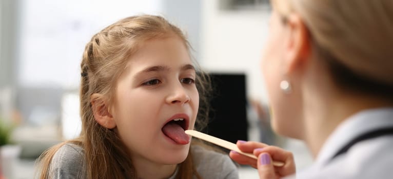 Portrait of pediatrician checking girls hurting throat with stick. Child open mouth for check up. Female doctor use tool for examination health. Medicine concept