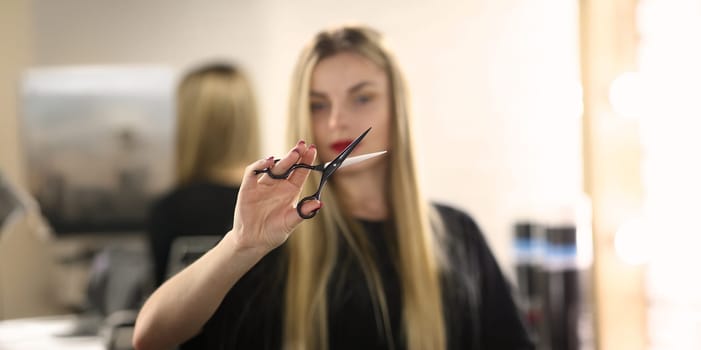 Portrait of female hairdresser holding scissors in hand, master ready to change client image. Beauty studio, self care and wellness concept