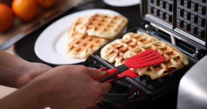 Close-up of waffle iron in kitchen, cooking homemade waffles. Woman preparing yummy breakfast for family