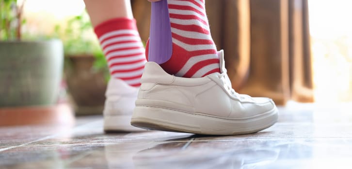 Close-up of person puts shoes white sneakers using shoehorn. Sport or casual shoes. Going for walk concept