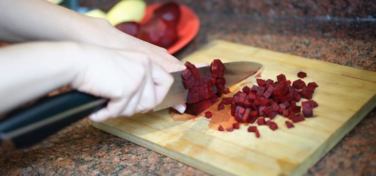 Close-up of woman cutting red beet root, ingredients for dish. Beetroot cube slice. Female preparing dinner. Cooking concept