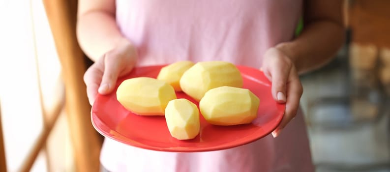 Close-up of female hands holding plate with raw peeled potatoes on it. Female preparing dinner, ingredients for dish. Cooking concept