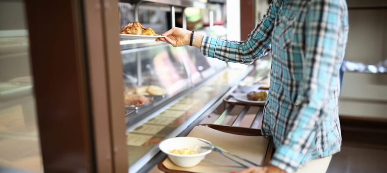 Close-up of woman taking plate with lunch in canteen. Visitor with tray select dish. Customer service with wide range of dishes. Self service restaurant