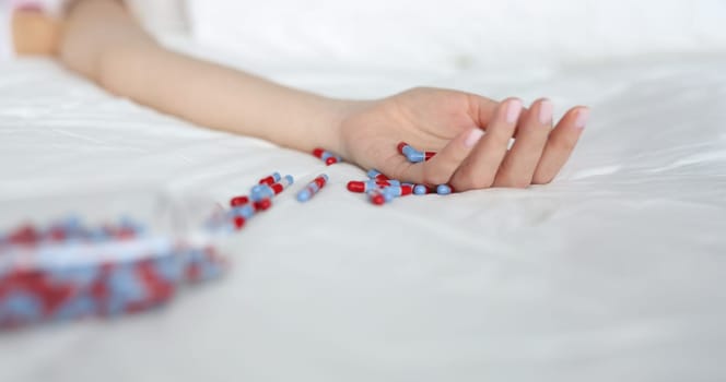 Close-up of young woman committing suicide by overdosing on medication. Overdose pills and addict. Female lying on bed and scattered pills on bedclothes