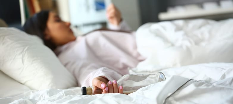 Close-up of drunk woman sleeping in bed and holding empty bottle. Person suffering from alcoholism. Female alcoholic and overdose or alcohol abuse concept