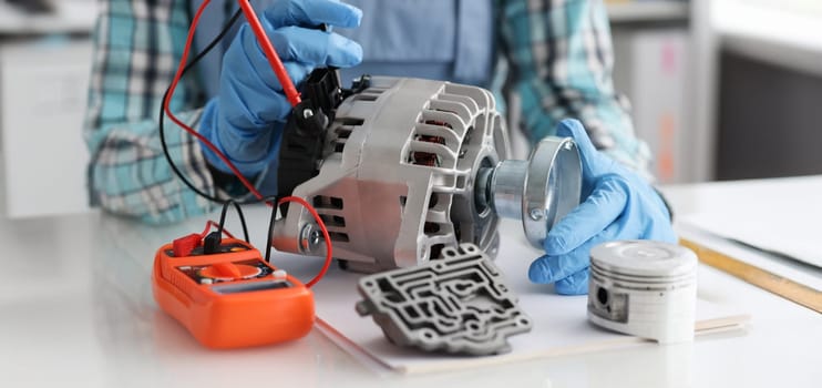 Close-up of handyman in gloves repairing automobile part and measuring voltage. Mechanic working in workshop. Generator repair. Car service concept