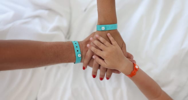 Close-up of parents and kid put hands all together. Friendly family and togetherness. Happy parenthood and childhood concept