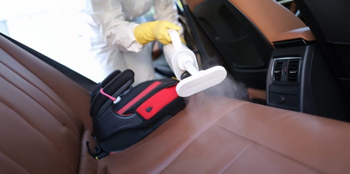 Close-up of worker in uniform cleanse car interior using steam cleaner with spray disinfectant. Disinfect machine and covid prevent concept