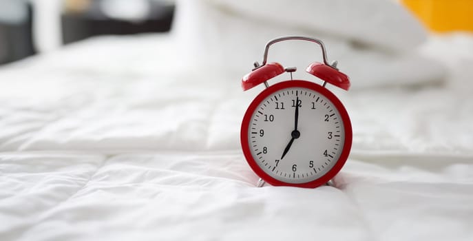 Close-up of red alarm clock at 7 oclock on bed. Early morning, daily regime and working day. Lack of sleep idea. Alarm-clock morning wake-up time concept