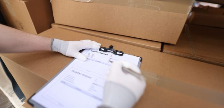 Close-up of courier service filling delivery receipt with client. Terms of delivery, receiving packages, parcels and cardboard boxes. Man filling form