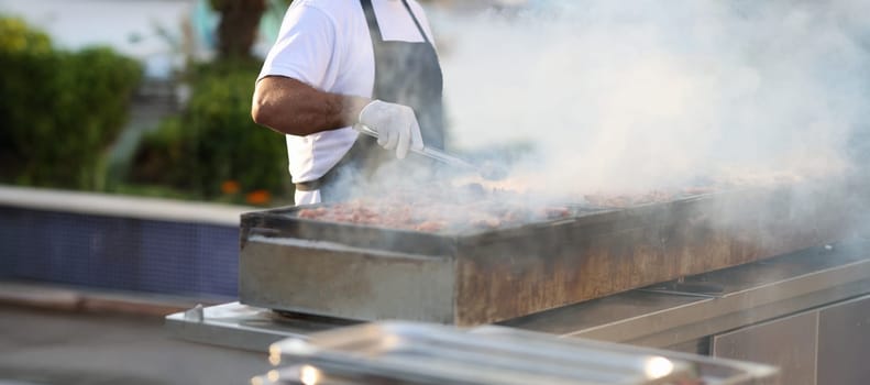 Close-up of chef cooking barbecue meat outdoors, summer lifestyle. Man grilling meat dish. Summer food festival, bbq event cooking