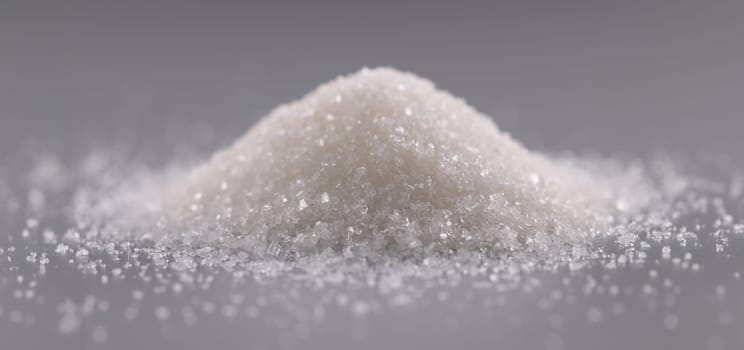 Close-up of pile of sugar crystals on grey surface, heap of sweet powder to add in dishes. Ingredient for cooking food, sweet crystalline substance concept