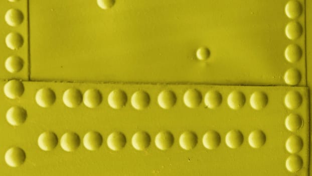 Fragment of a wall covered with sheet metal with rivets. Yellow abstract metal background.