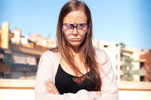 Caucasian business woman wearing glasses, looking serious with arms crossed at camera standing in an outdoor workspace. Front view of a young lawyer with negative expression staring