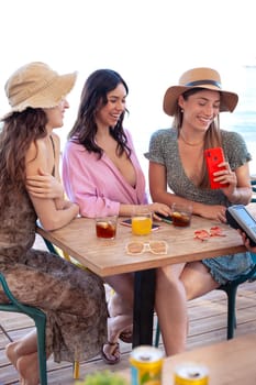 Three happy friends who are in the restaurant with drinks, pay with contactless payment via mobile phone app.Vertical