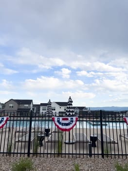 Castle Rock, Colorado, USA-July 6, 2024-A neighborhood pool area decorated with a red, white, and blue bunting flag hanging on a black iron fence. Houses and loungers are visible in the background, creating a festive and inviting atmosphere.