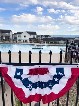 Castle Rock, Colorado, USA-July 6, 2024-A neighborhood pool area decorated with a red, white, and blue bunting flag hanging on a black iron fence. Houses and loungers are visible in the background, creating a festive and inviting atmosphere.