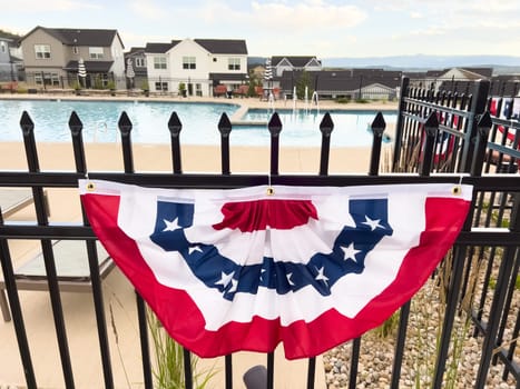 Castle Rock, Colorado, USA-July 6, 2024-A neighborhood pool area decorated with a red, white, and blue bunting flag hanging on a black iron fence. Houses and loungers are visible in the background, creating a festive and inviting atmosphere.
