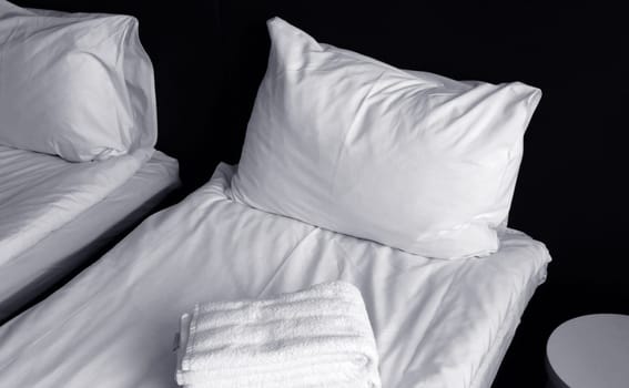 The bed is covered with a fresh white sheet, a white pillow, and a laying towel. Fragment of a cozy bedroom.