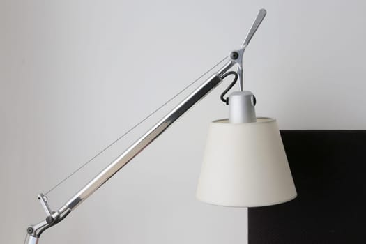 Close-up of a burning table lamp with a bracket near the bed. Lamp shade. Vintage table lamp against the wall.