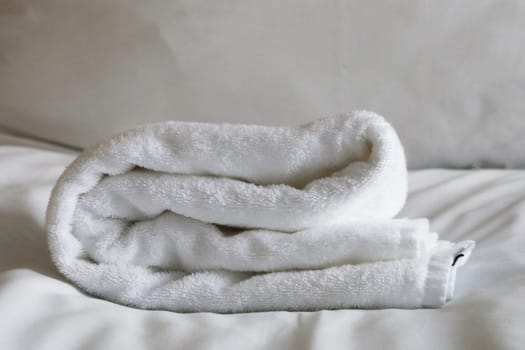 A large terry white towel lies on white bed linen.