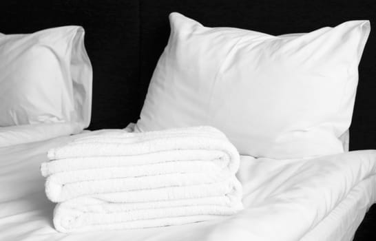 Two pillows, folded terry white towels on a sheet on a black background.