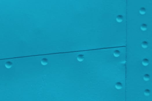 Fragment of a wall covered with sheet metal with rivets. Blue abstract metal background.