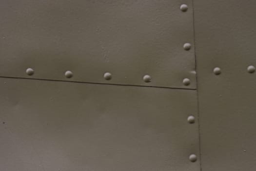 The surface of a metal wall with green rivets. Airplane fuselage painted green.