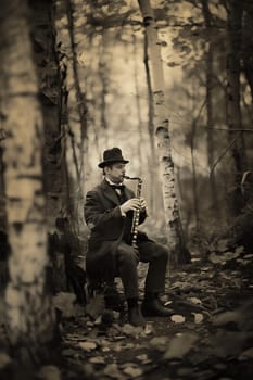 A man in a hat and a suit is sitting in a forest, playing a clarinet. The image has a vintage feel to it, and the man's attire and instrument suggest that he is a musician