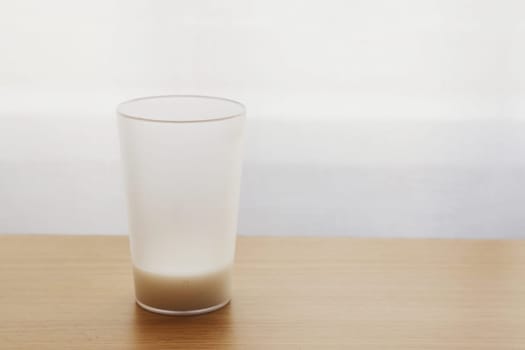 A half-full glass of drink stands on a brown table opposite the window.