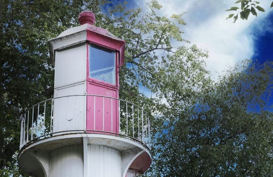 Top of lighthouse, door, window, fence against sky and forest.