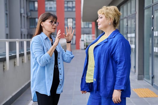 Two mature businesswomen talking at meeting, serious confident women outdoor, office center, urban background. Work, business, communication, confidence, success, maturity concept