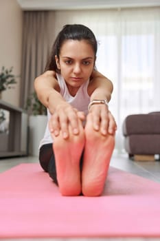 Sporty Caucasian woman worm up by stretching her body on pink exercise mat at home