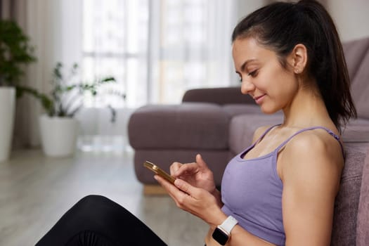 sporty woman sitting and using smartphone after her home workout at home