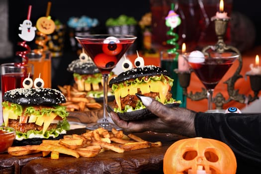  A witch's hand takes a Witch cocktail with eyeballs in a martini glass from the Halloween party table.