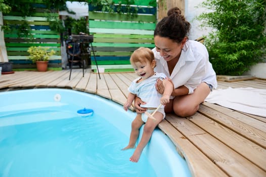 A joyful moment as a mother and her toddler sit by the pool, splashing and having fun. Perfect family bonding time on a sunny summer day.