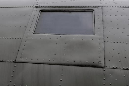 Fuselage fragment of an old military airplane with a square illuminator, bottom view. Cladding and window of the airplane.
