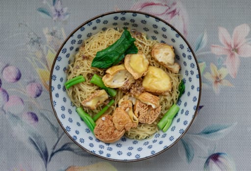 Top view of Egg Noodles with Fried tofu and Chinese kale without Soup sprinkled with Fried garlic in Ceramic bowl. Space for text, Selective focus.