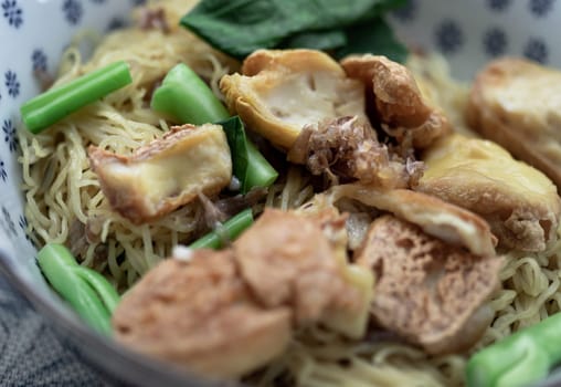 Close-up of Egg Noodles with Fried tofu and Chinese kale without Soup sprinkled with Fried garlic in Ceramic bowl. Space for text, Selective focus.