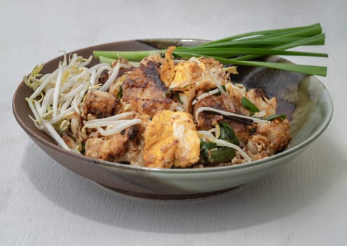 Stir-fried soft turnip cake or Fried radish cake (chai tow kway) with bean sprout and chives on ceramic plate. Thai - Chinese food called Kanom Pak kad or Char Koay Kak, Space for text, Selective focus.
