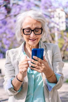 portrait of a lively mature woman smiling happy while typing on mobile phone, concept of technology of communication and modern lifestyle in adulthood